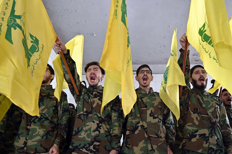 Hezbollah fighters in battledress saluting alongside the organisations banners.