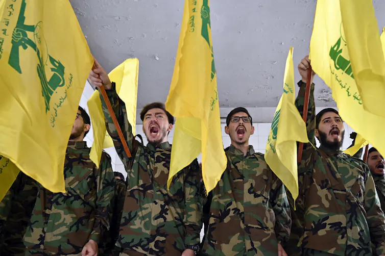 Hezbollah fighters in battledress saluting alongside the organisations banners.