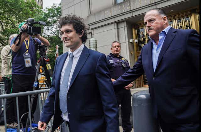 Sam Bankman Fried, crypto exchange founder, leaving court, cameras and police in the background. 