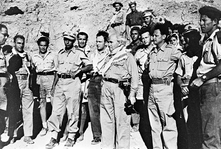 Several men in military uniform standing in a desert-like terrain.