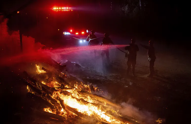 Firefighters seen spraying water onto buring logs.