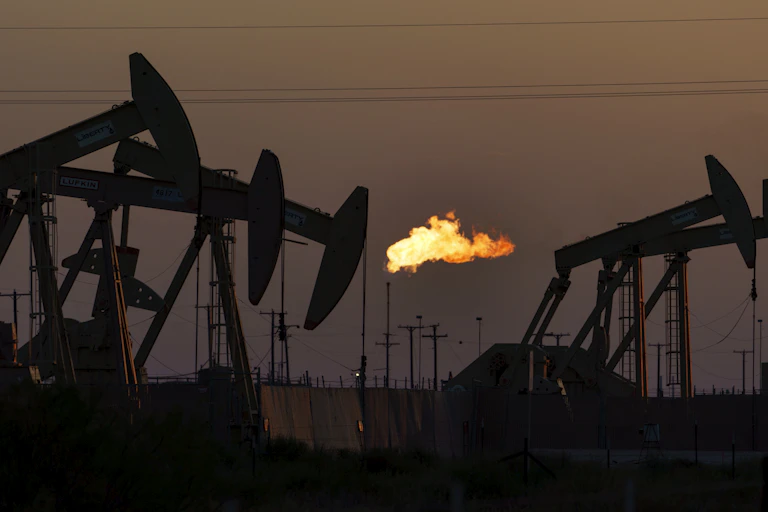 Pumpjacks and a flame seen burning against the night sky.
