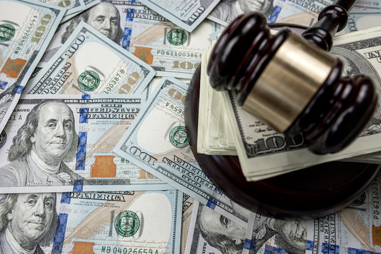 A stack of paper money is under a gavel.