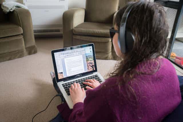 A woman wearing dark sunglasses and headphones types on a laptop