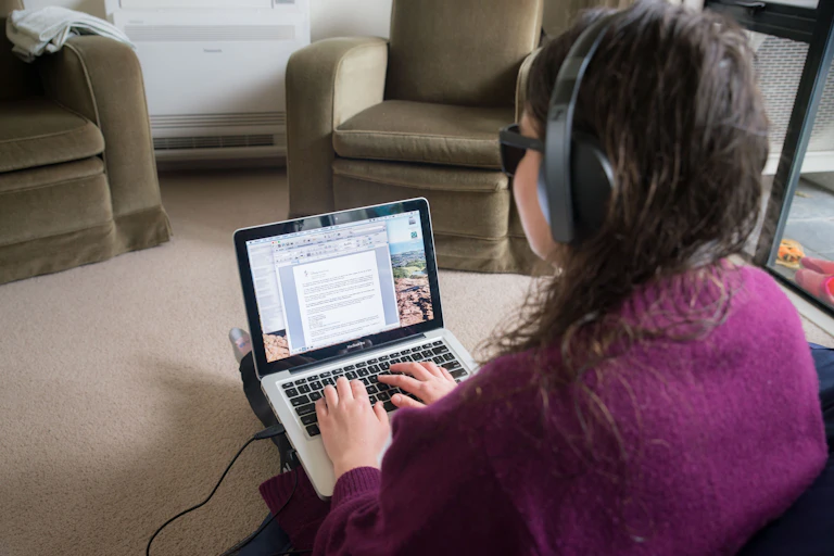A woman wearing dark sunglasses and headphones types on a laptop