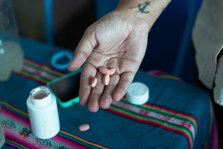 Hand holding orange PrEP pills above a clothed table with an open pill bottle