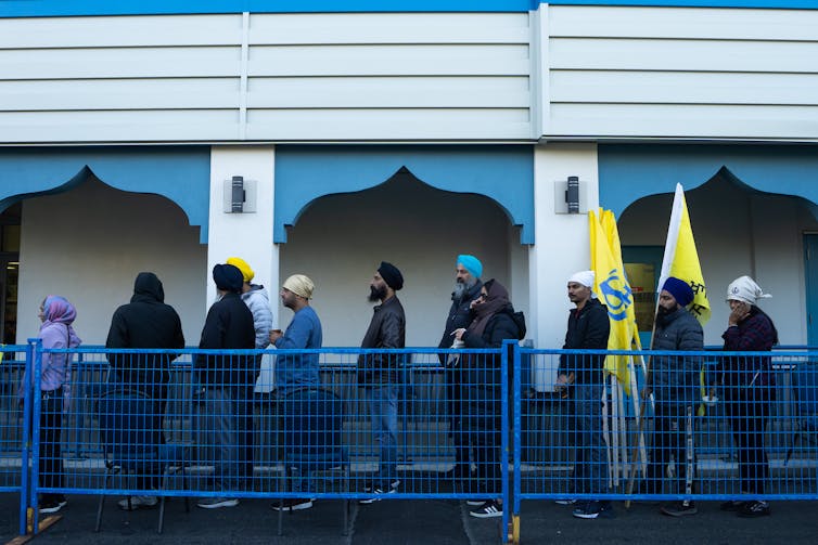 Sikh people line up outside a building.