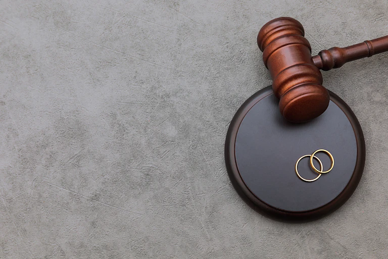 A gavel seen next to two wedding rings.