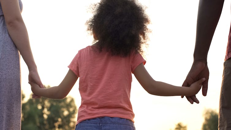 A child in the middle holds two different adult hands. 