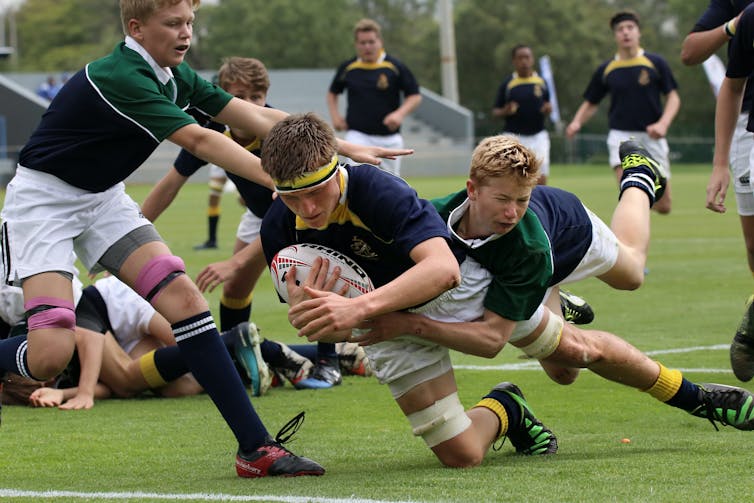 One school boy tackles another in a rugby game.