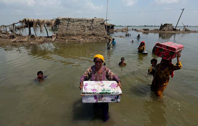 Women carry belongings salvaged from their flooded home after monsoon rains, in the Qambar Shahdadkot district of Sindh Province, of Pakistan, Sept. 6, 2022