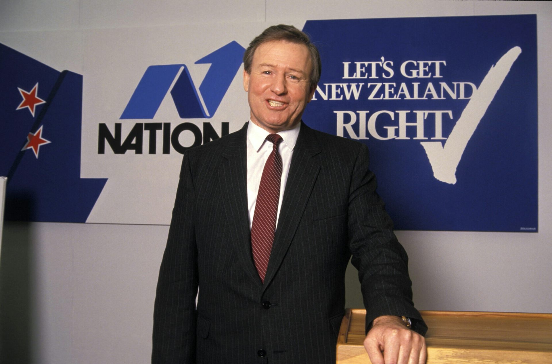 Jim Bolger in front of old National Party sign.