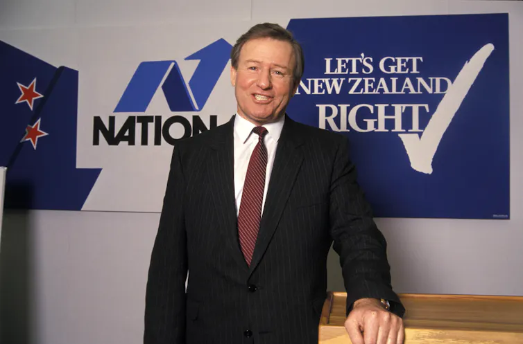 Jim Bolger in front of old National Party sign.