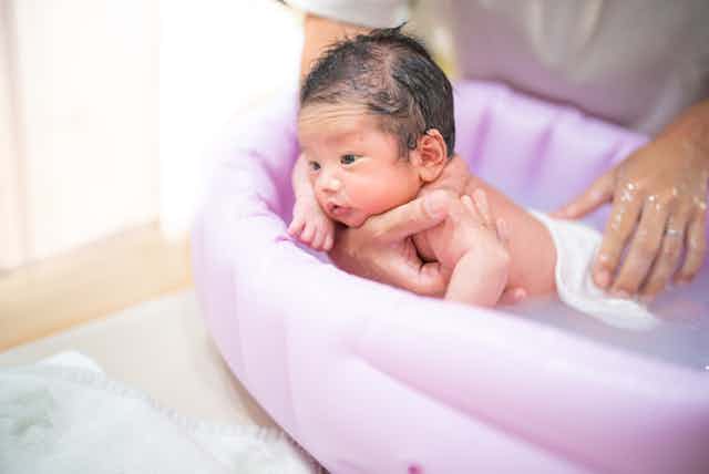 Father bathing newborn baby in inflatable bath
