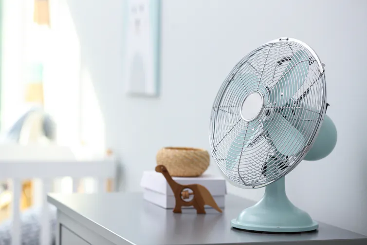 Fan on chest of drawers, cot in background