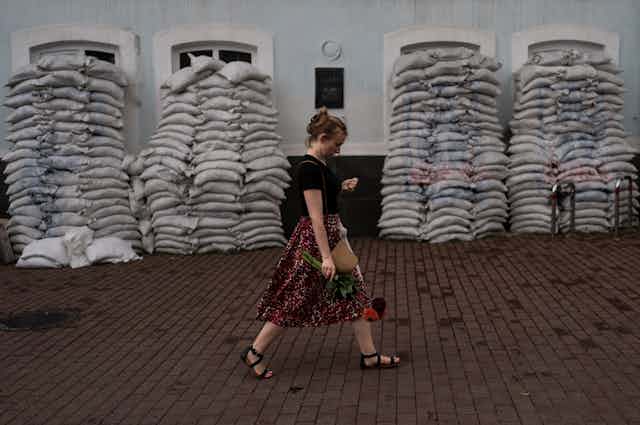 Woman holding flowers walks past sandbags protecting a building.