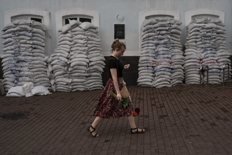 Woman holding flowers walks past sandbags protecting a building.