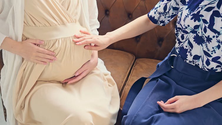 A woman touches a pregnant woman's stomach with.