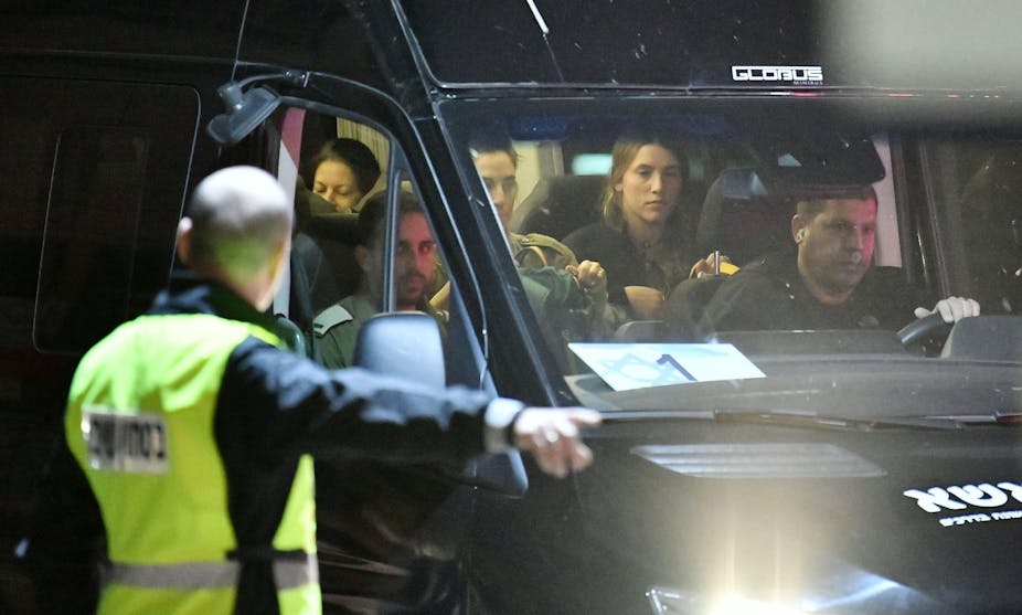 A man in a hi-viz jacket directs a minibus with several people inside