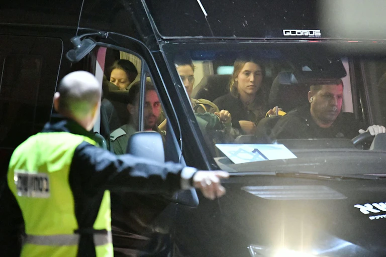 A man in a hi-viz jacket directs a minibus with several people inside