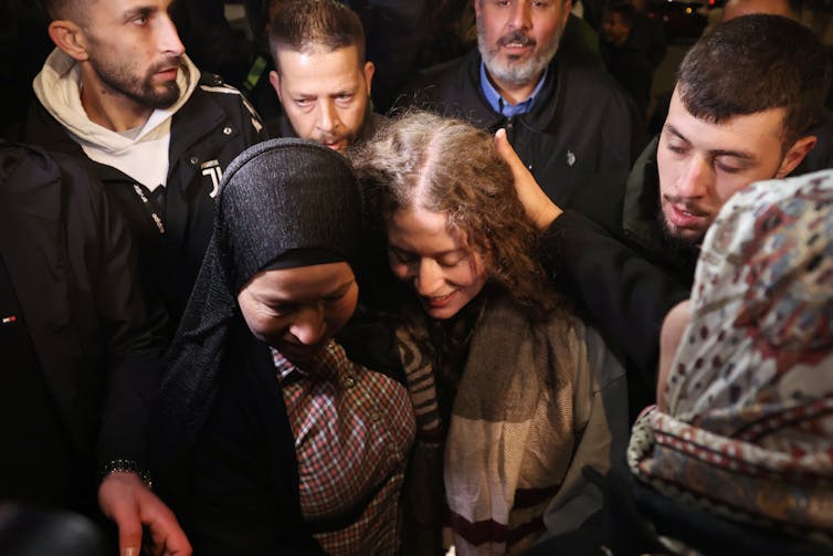 A woman in a headscarf is embraced by another woman, surrounded by men.
