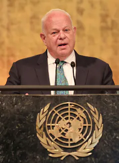 A man in a suit speaks behind a podium with the United Nations logo on it