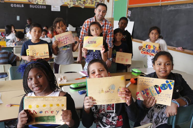 A classroom of kids hold up their handmade gratitude journals showing words like 'freedom,' 'love' and 'brother.'