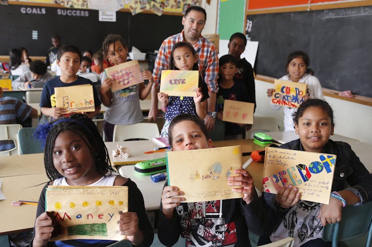 A classroom of kids hold up their handmade gratitude journals showing words like « freedom, » « love » and « brother. »