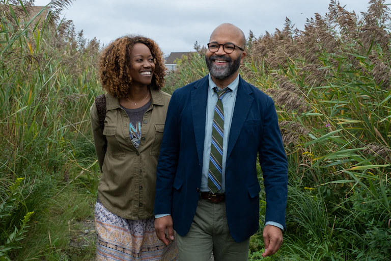 A Black woman smiles while looking at a Black man who looks forward.