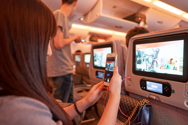 A woman taking a photo of the screen on the back of an airline seat with her cellphone