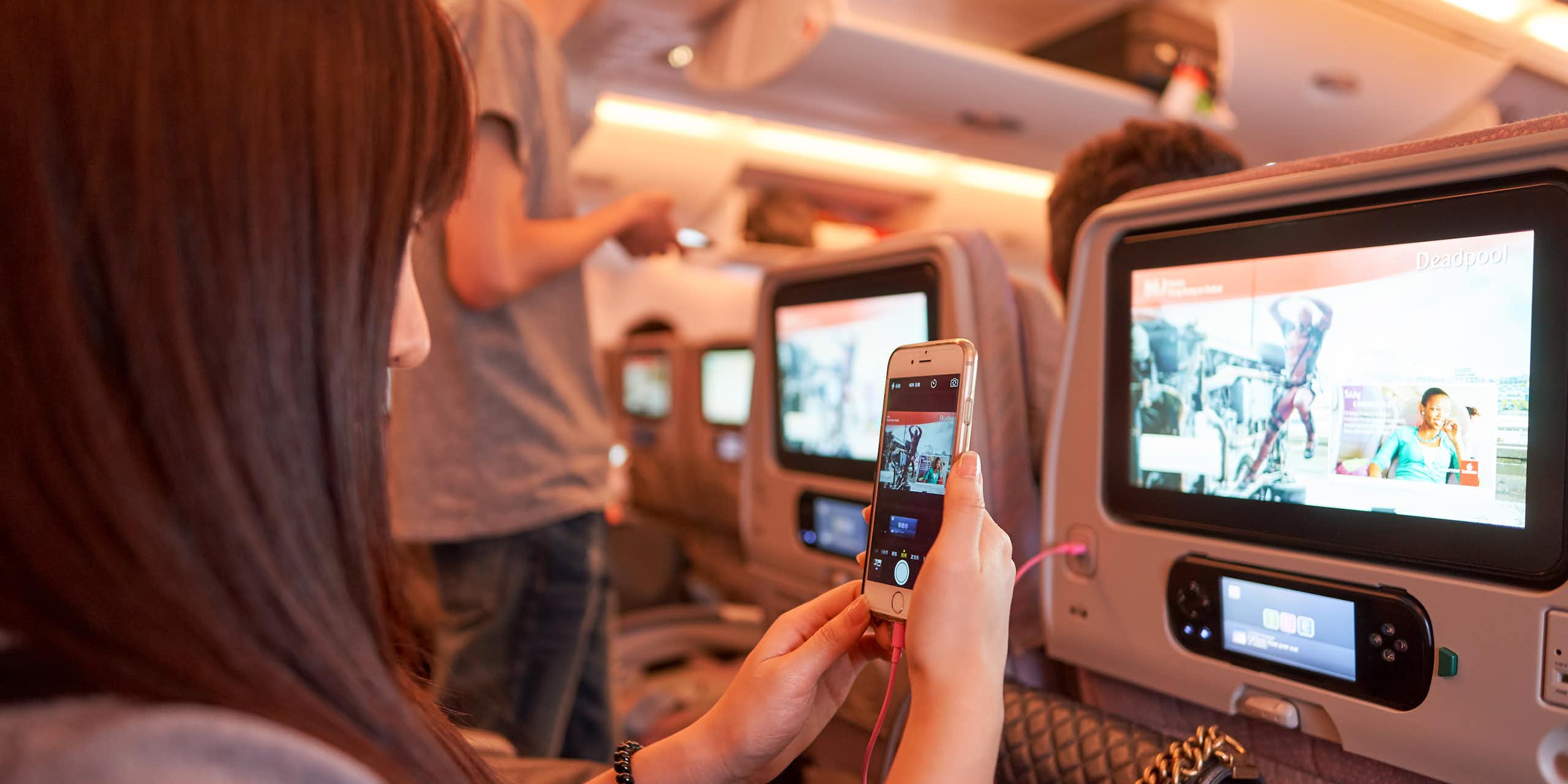 A woman taking a photo of the screen on the back of an airline seat with her cellphone