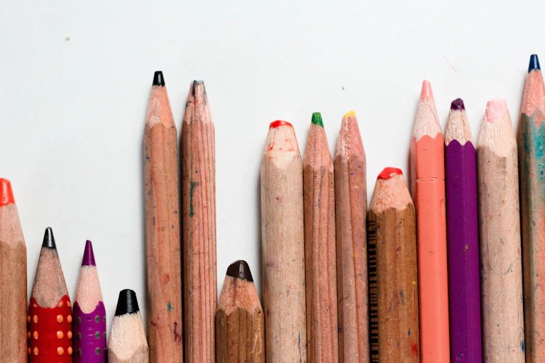 A row of coloured pencils in different states of use - some sharp some blunt.