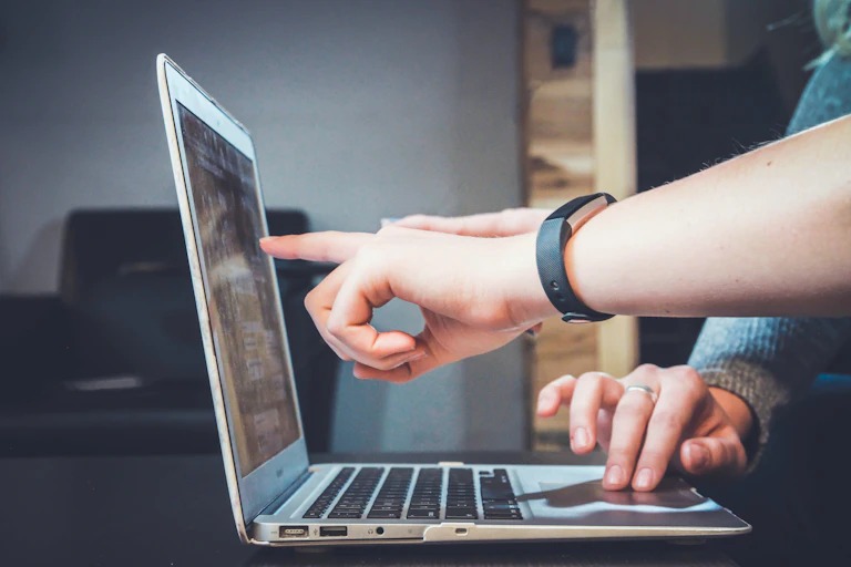 Two people use a laptop together and point and the screen.