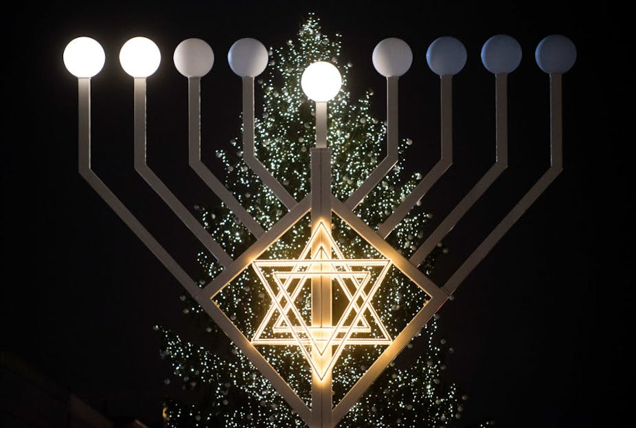 Lights in the shape of a six-pointed star positioned in front of large lamppost-like structures and a decorated tree. 