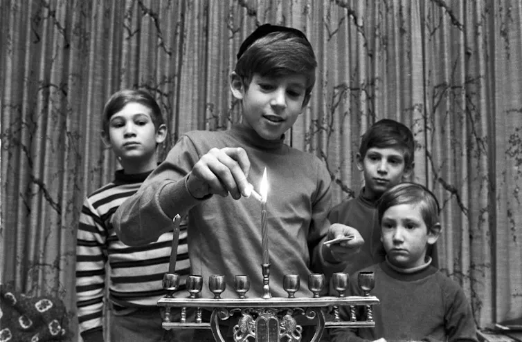 A black and white photo of four young boys, three of them looking on as the eldest lights a candle.