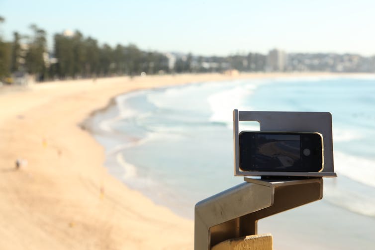 CoastSnap stainless steel camera cradle with smartphone placed in it, overlooking Manly beach