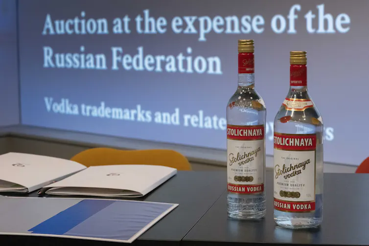 Two vodka bottles sit in front of a jumbo screen that reads: Auction at the expense of the Russian Federation.