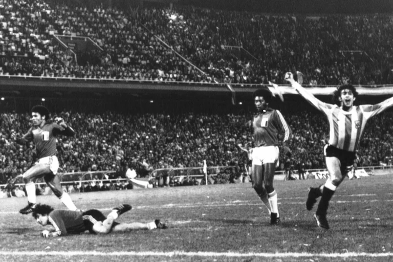 Um jogador da seleção argentina comemora um gol enquanto dois jogadores peruanos e o goleiro no chão observam