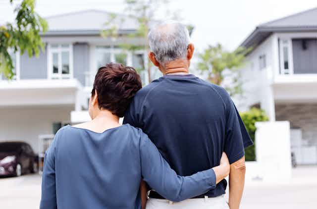 An older couple with their backs to the camera in front of a house