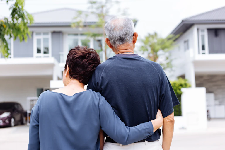 An older couple with their backs to the camera in front of a house