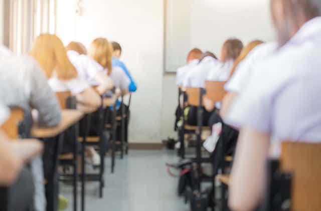 Students in school uniform sit an exam in an exam hall.