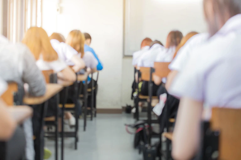Students in school uniform sit an exam in an exam hall.