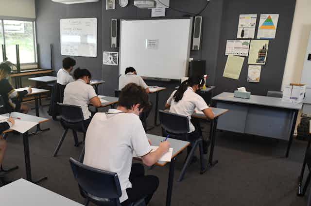 Students sit at separated desks to do an exam in a classroom.