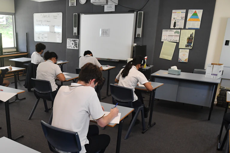 Students sit at separated desks to do an exam in a classroom.