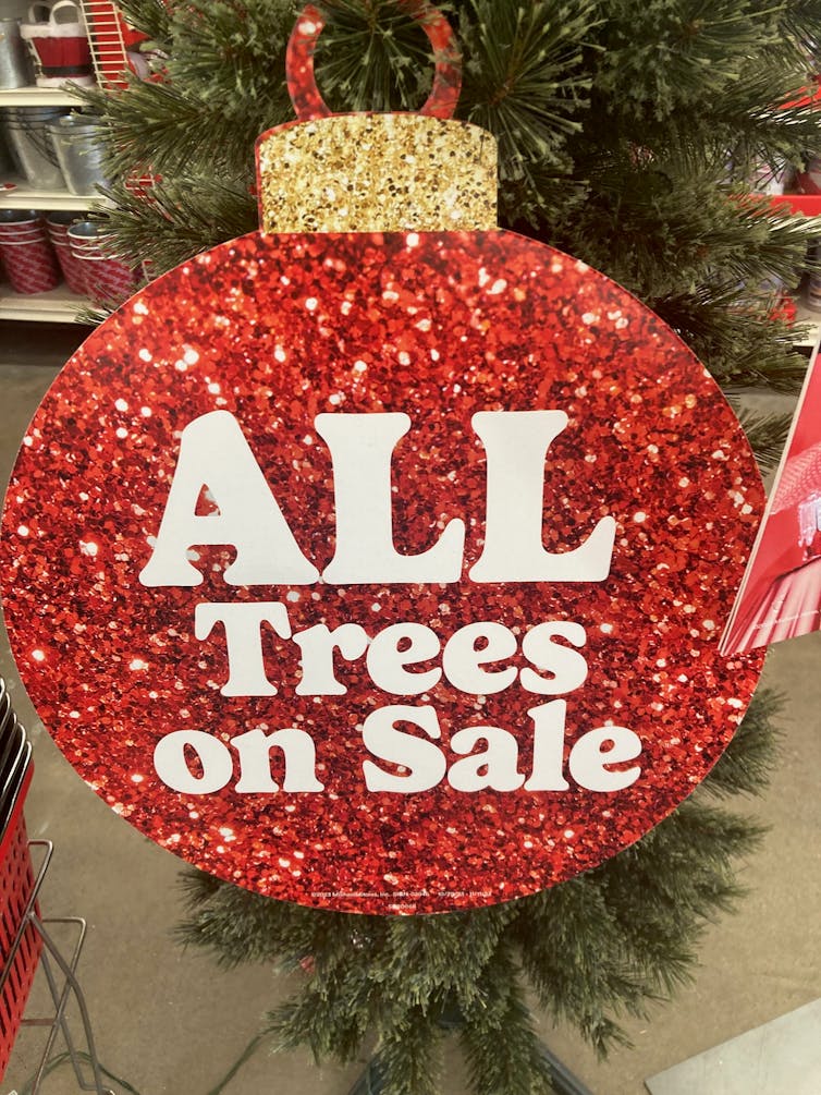 In a store, a sign in the shape of a Christmas tree ornament reads 'All trees on sale.'