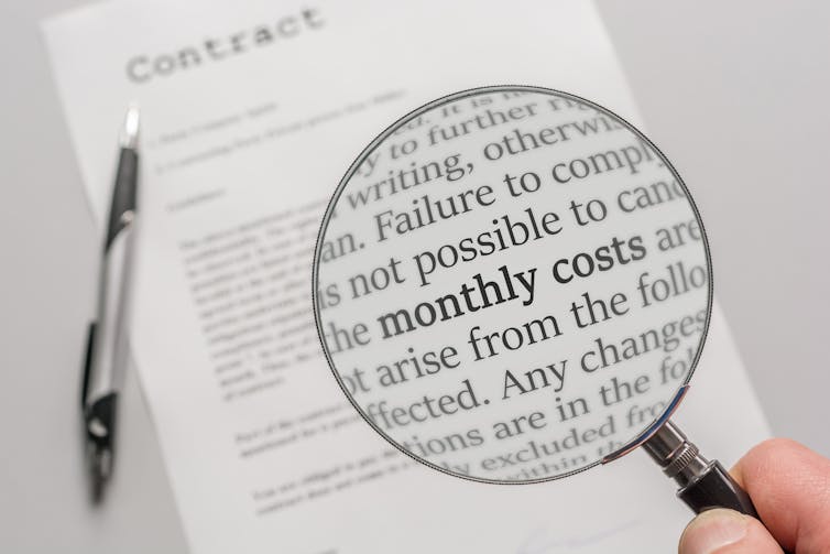 A hand holding a magnifying glass over a page of a contract, highlighting some specific detail