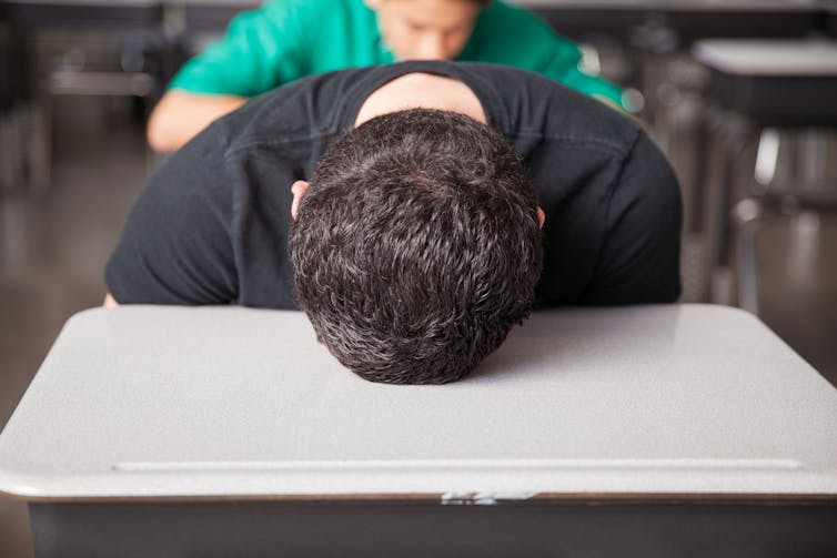 A boy puts his head on a desk.