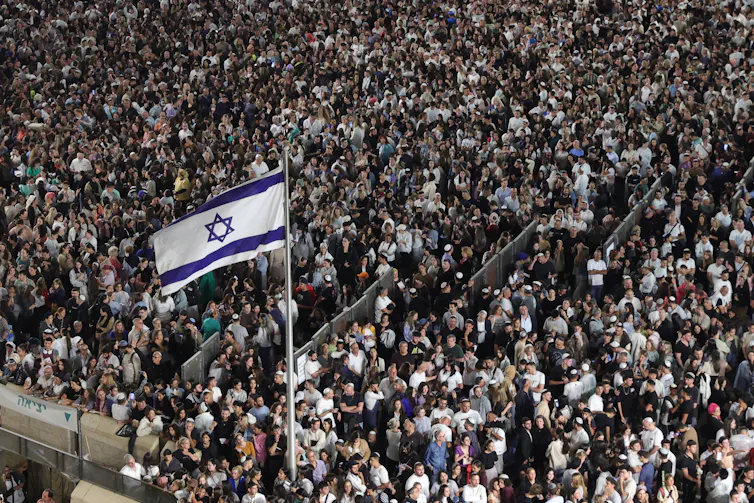 A dense crowd of people around an Israeli flag
