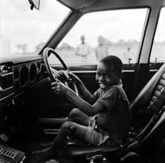 A boy laughs while both hands are on the steering wheel of a racing car.
