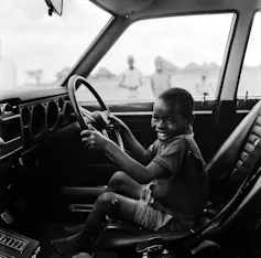 Un niño ríe mientras tiene ambas manos en el volante de un coche de carreras.